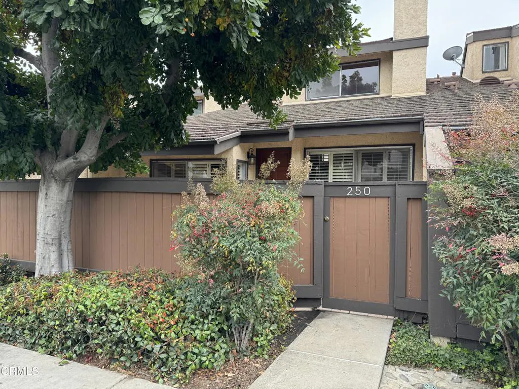 Exterior view of a two-story tan house with brown trim and a brown fence with the number 250 above the gate.