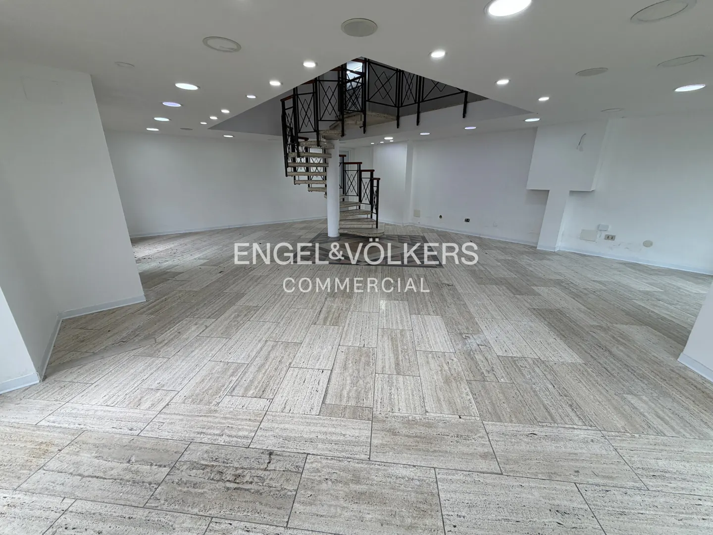 Bright, empty commercial space with white walls, tile floor, and a spiral staircase with black railings leading to an upper level.