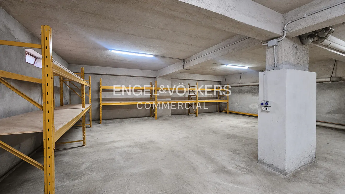A commercial space with concrete floors, walls, and ceiling. Yellow metal shelving units line the walls.