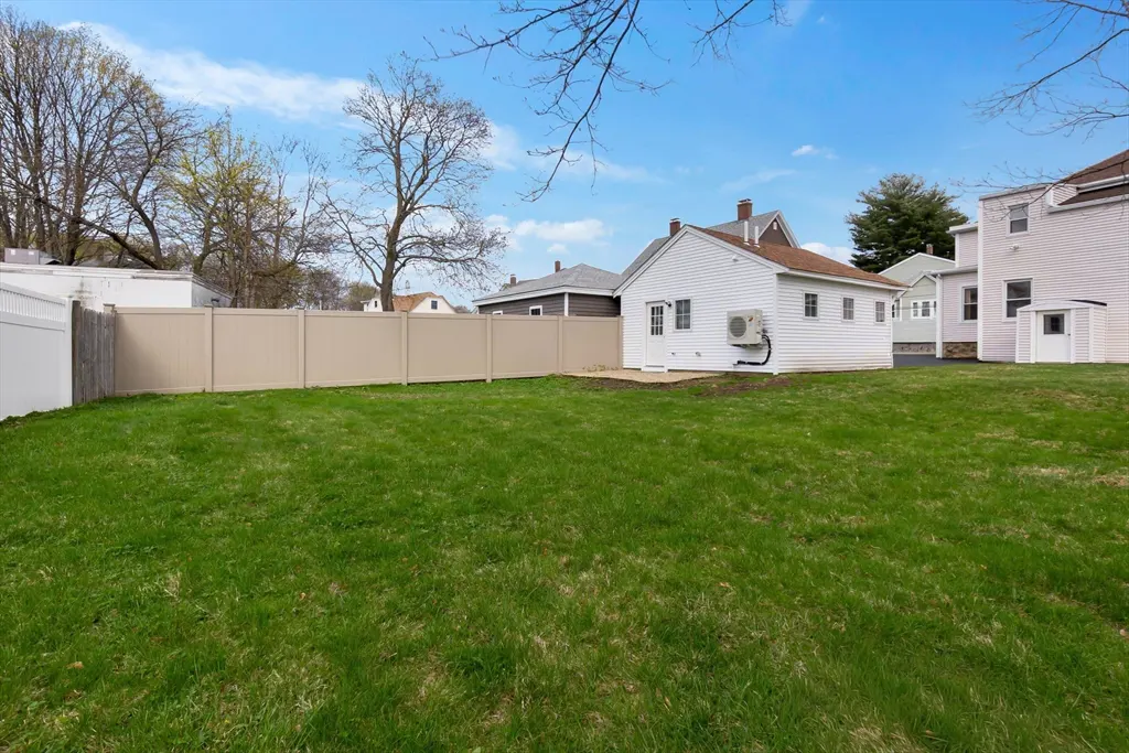 A large green lawn is enclosed by a beige fence, with a white house and blue sky in the background.