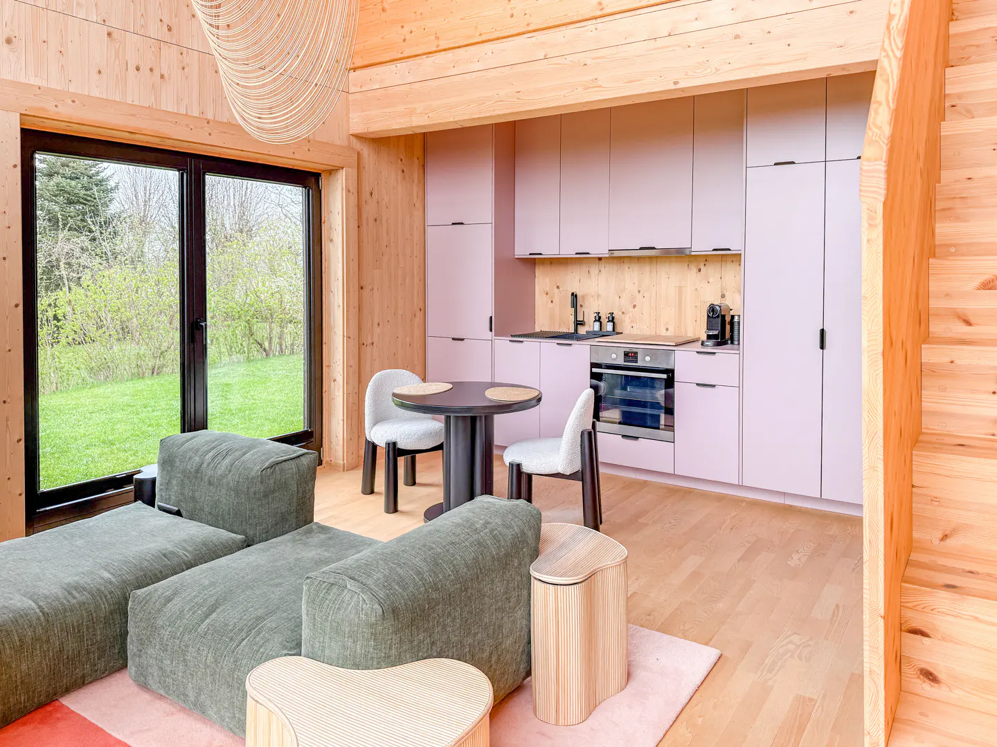 Interior view of a modern cabin with wood walls, pink cabinets, green sofa, and a black framed window.