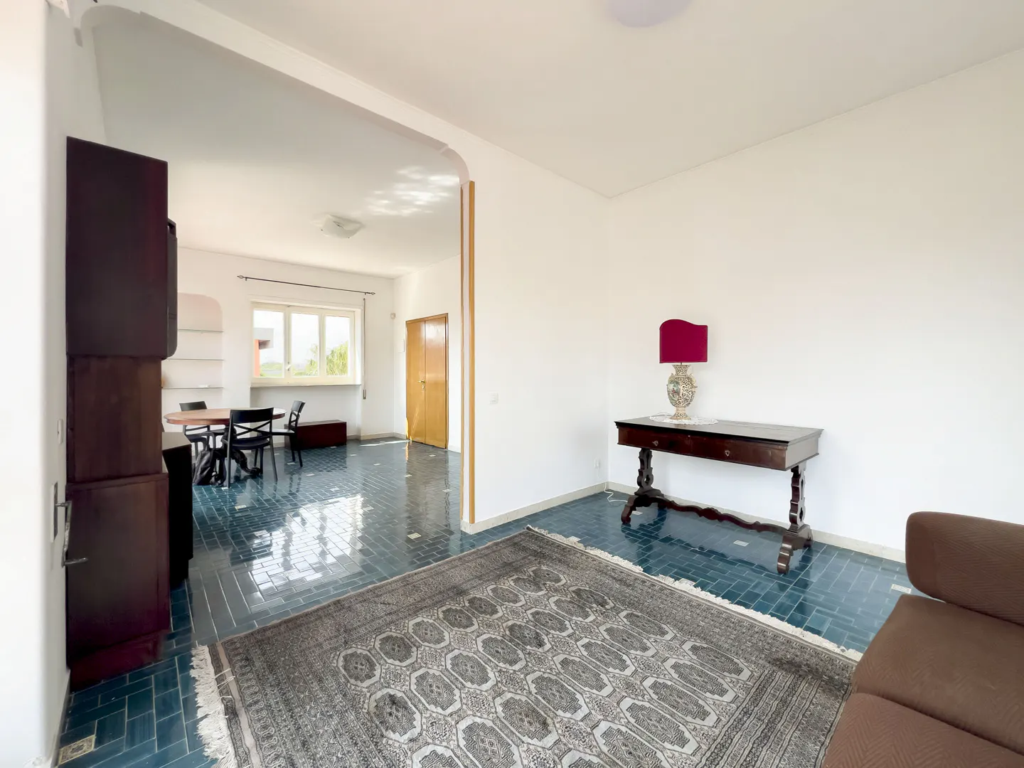 Interior view of a room with blue tile floors, a patterned rug, and a dark wood table with a red lamp.