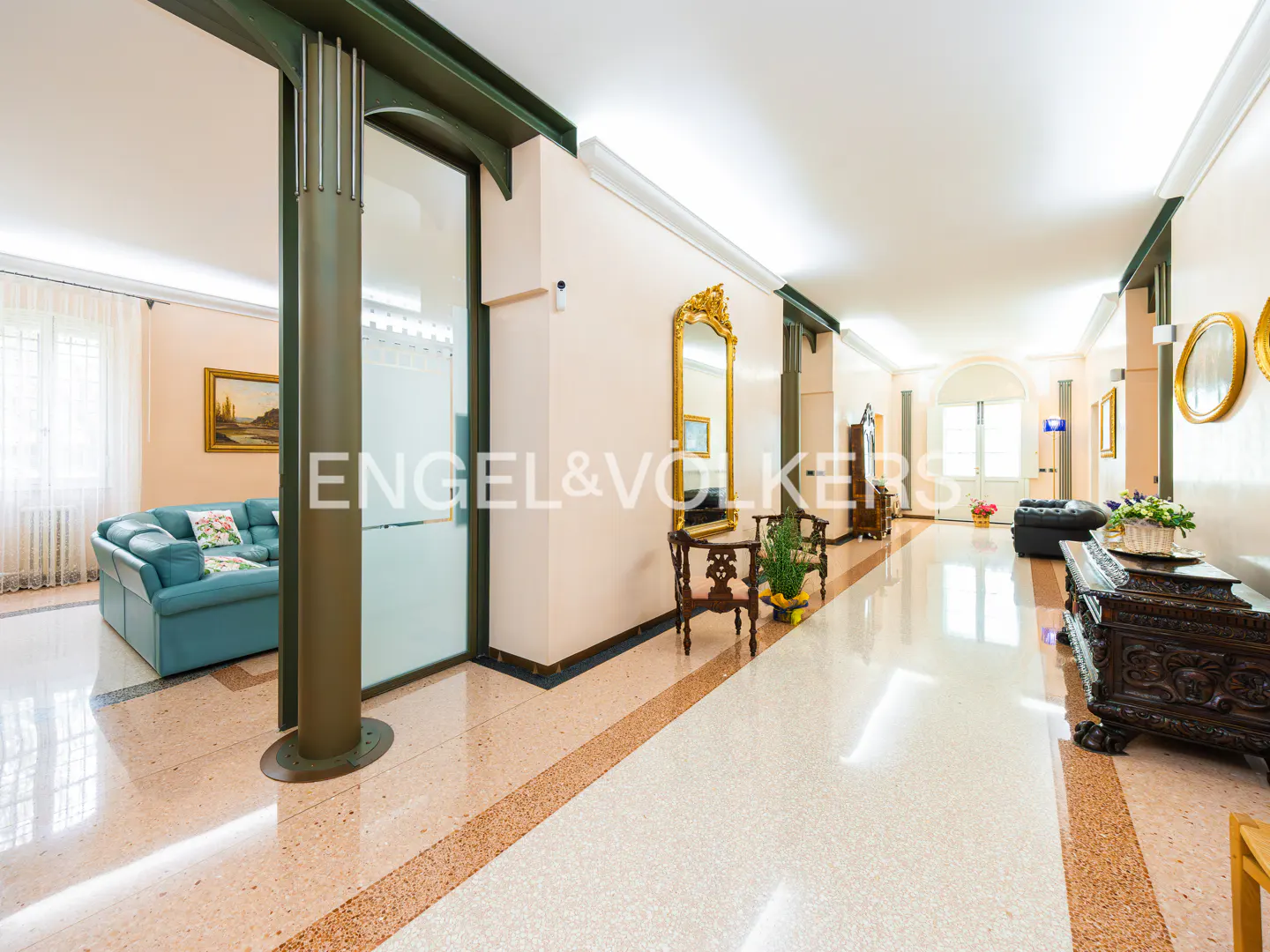 A long hallway with a marble floor, gold mirrors, and a blue couch.