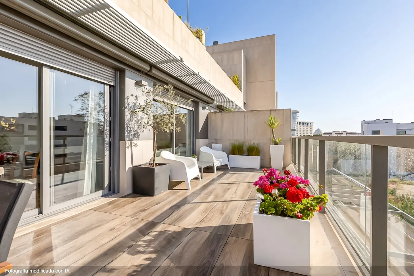 A modern balcony with wood-look tile, white chairs, and potted plants. A glass railing offers city views.