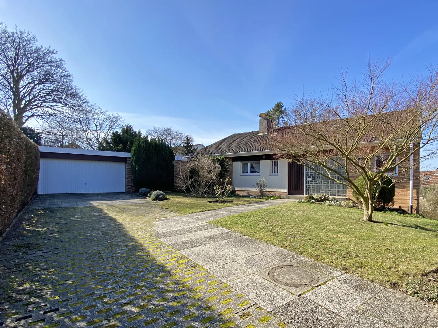 A single-story house with a garage, a driveway, and a lawn on a sunny day.