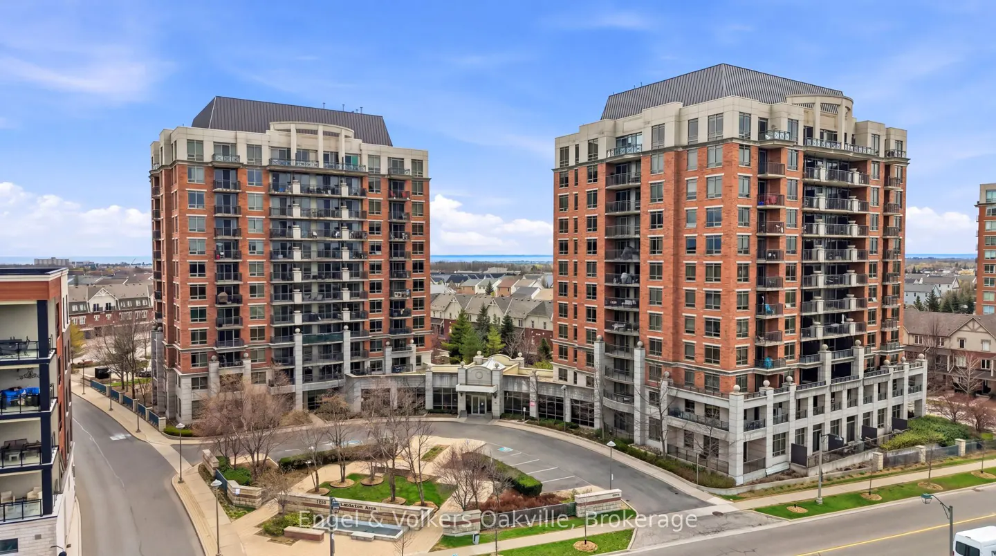 Two tall, red brick apartment buildings with balconies, connected by a central entrance, under a blue sky.