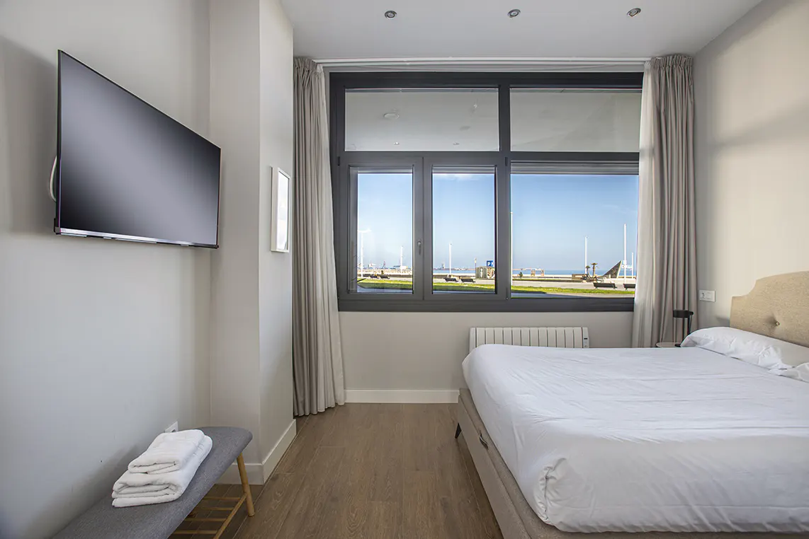 Bedroom with a large window view of the ocean, a flat screen TV, and a bench with folded towels.