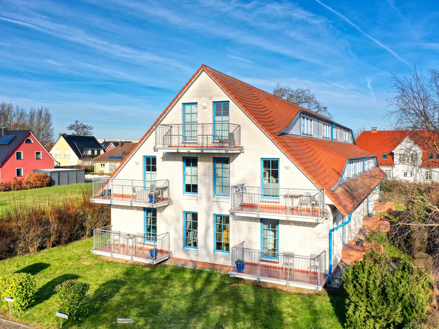 A white brick house with a red tile roof and blue-framed windows and balconies on a sunny day.