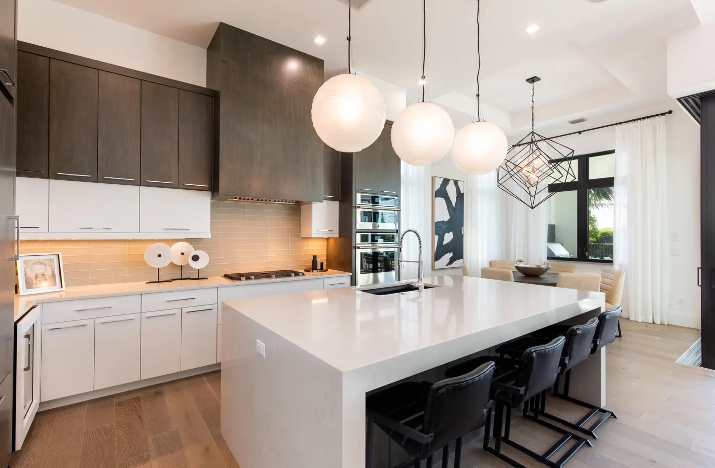 A modern kitchen with white cabinets, a large island with black stools, and globe pendant lights.