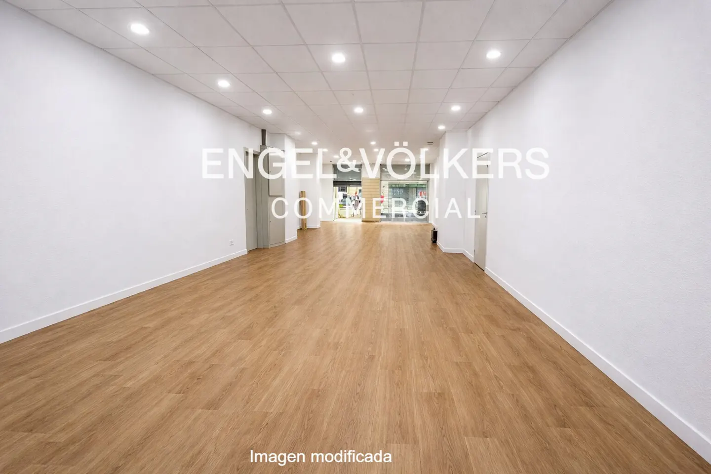 Empty commercial space with light wood floors, white walls, and recessed lighting. Engel & Völkers logo is superimposed on the image.