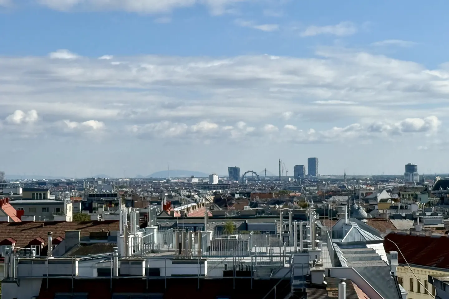 Cityscape view of Vienna, Austria, with red rooftops and modern buildings under a cloudy blue sky.