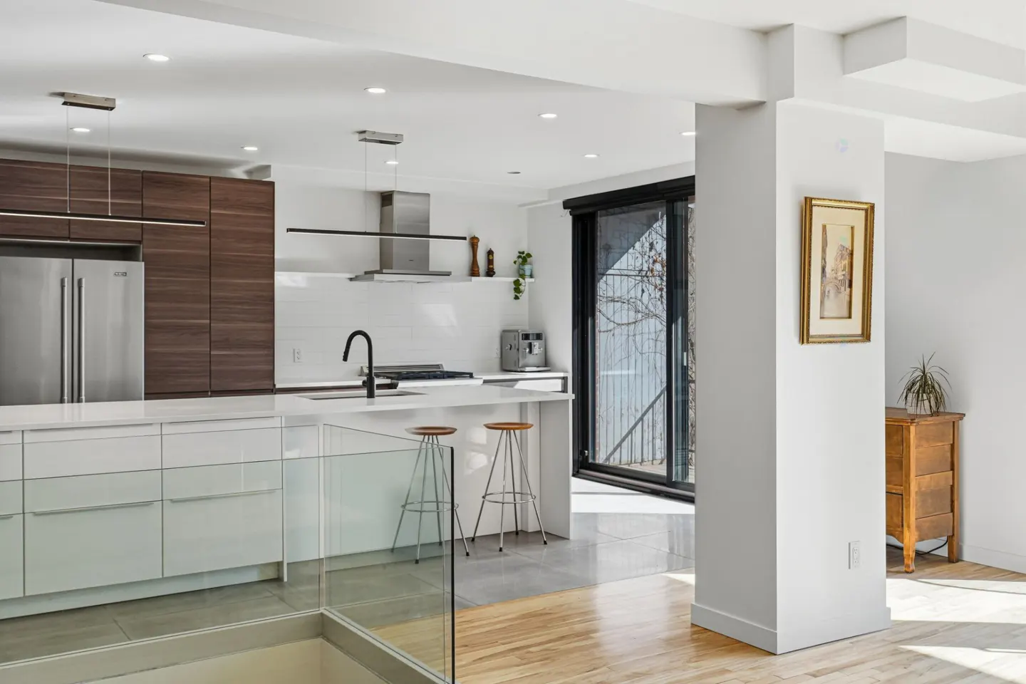 Bright, modern kitchen with white cabinets, stainless steel appliances, and wood accents. Stools at the island and a sliding glass door to the outside.
