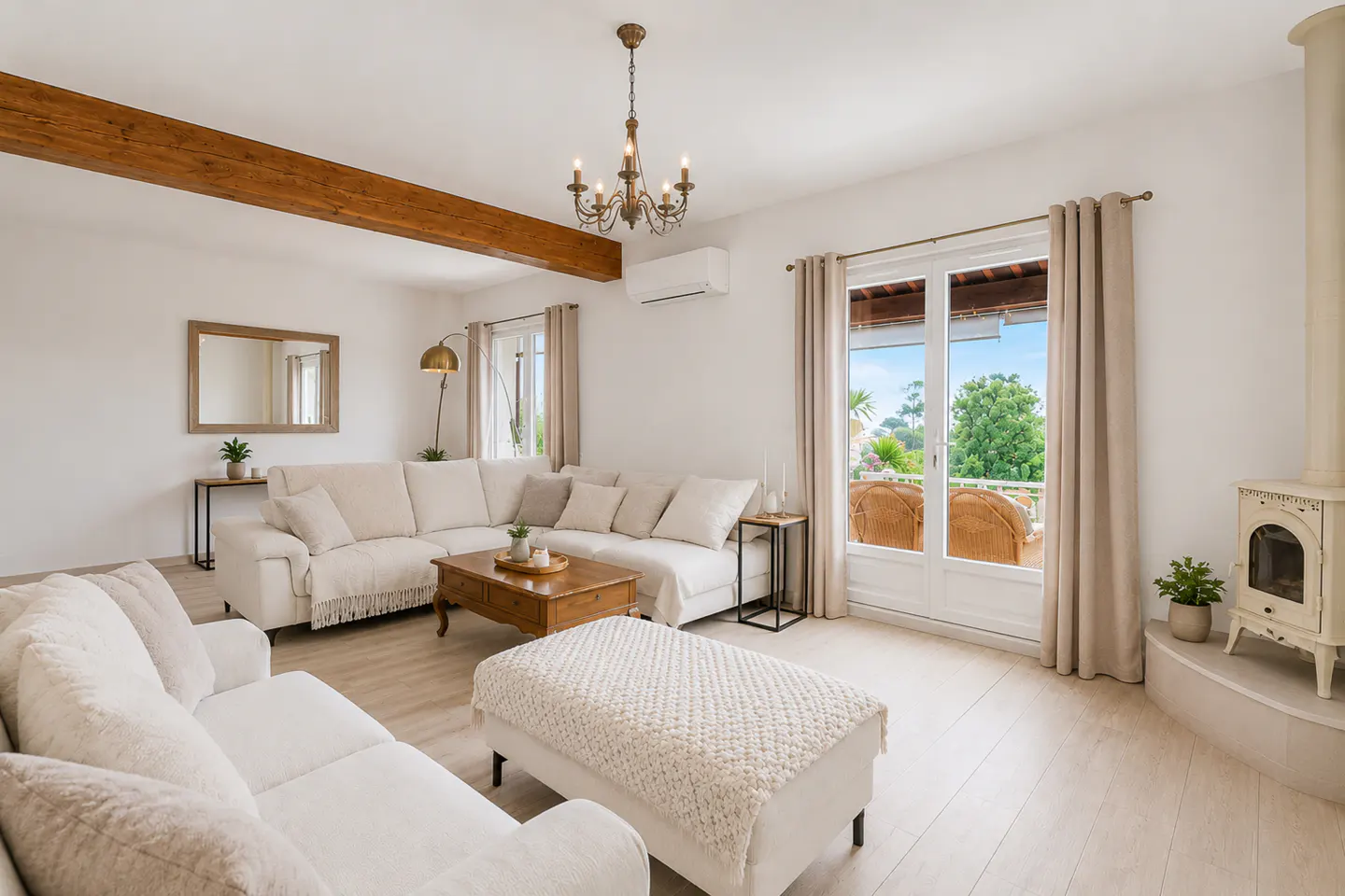 Bright living room with white sofas, wood floors, and a chandelier. A balcony with a view is visible through the glass doors.