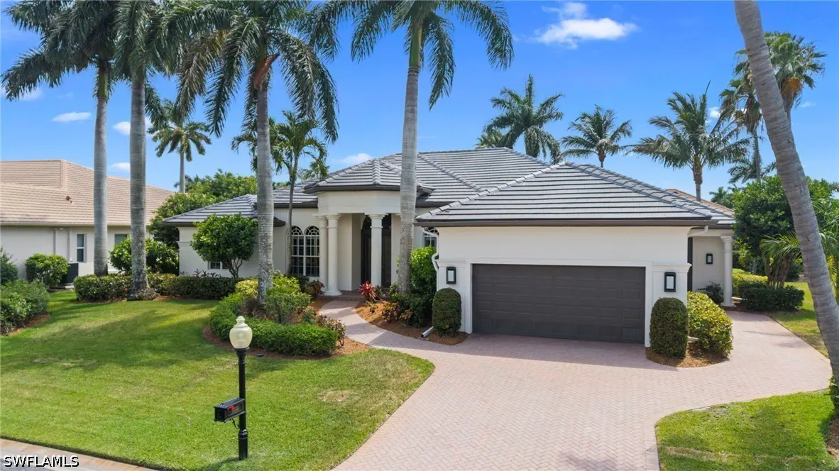 Beige one-story house with a gray roof, dark garage door, and palm trees in the front yard.