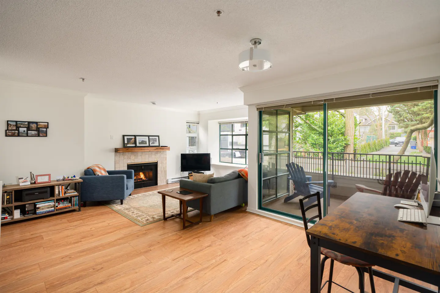 Bright living room with wood floors, fireplace, blue armchair, gray sofa, and sliding glass doors to a balcony with chairs.