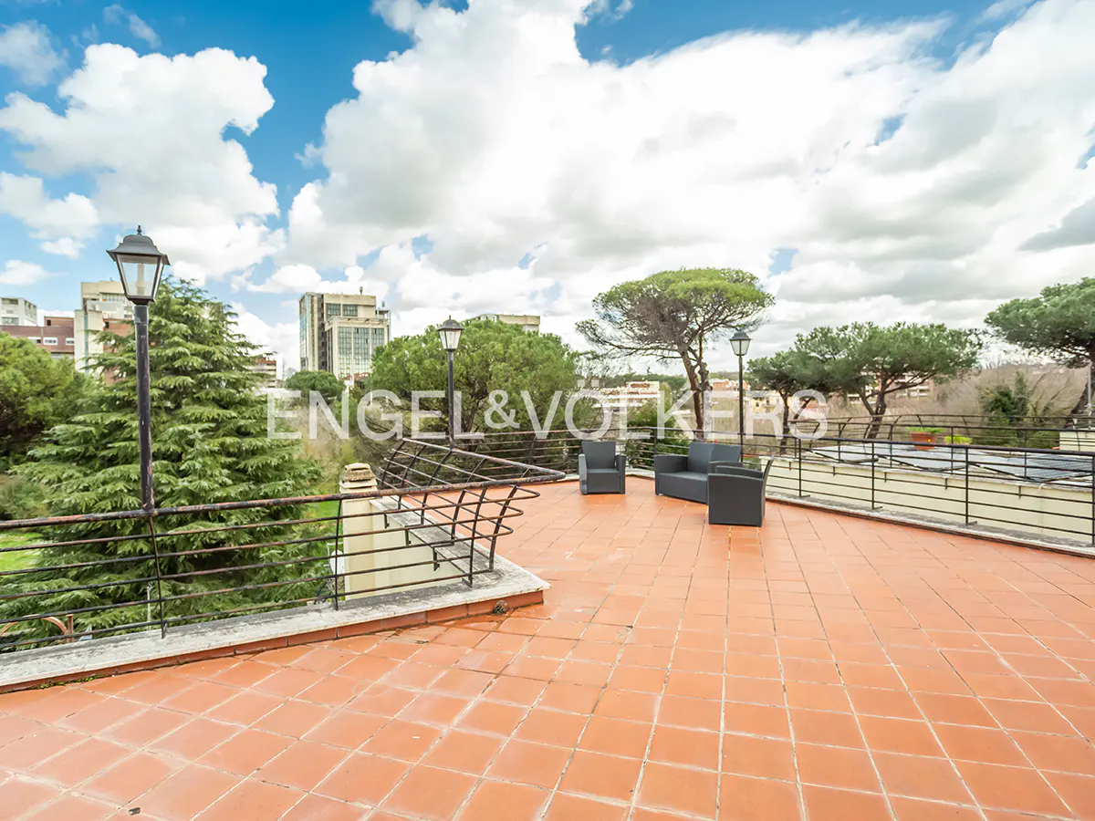 Spacious rooftop terrace with terracotta tiles, black metal railings, outdoor seating, and views of trees and city buildings.