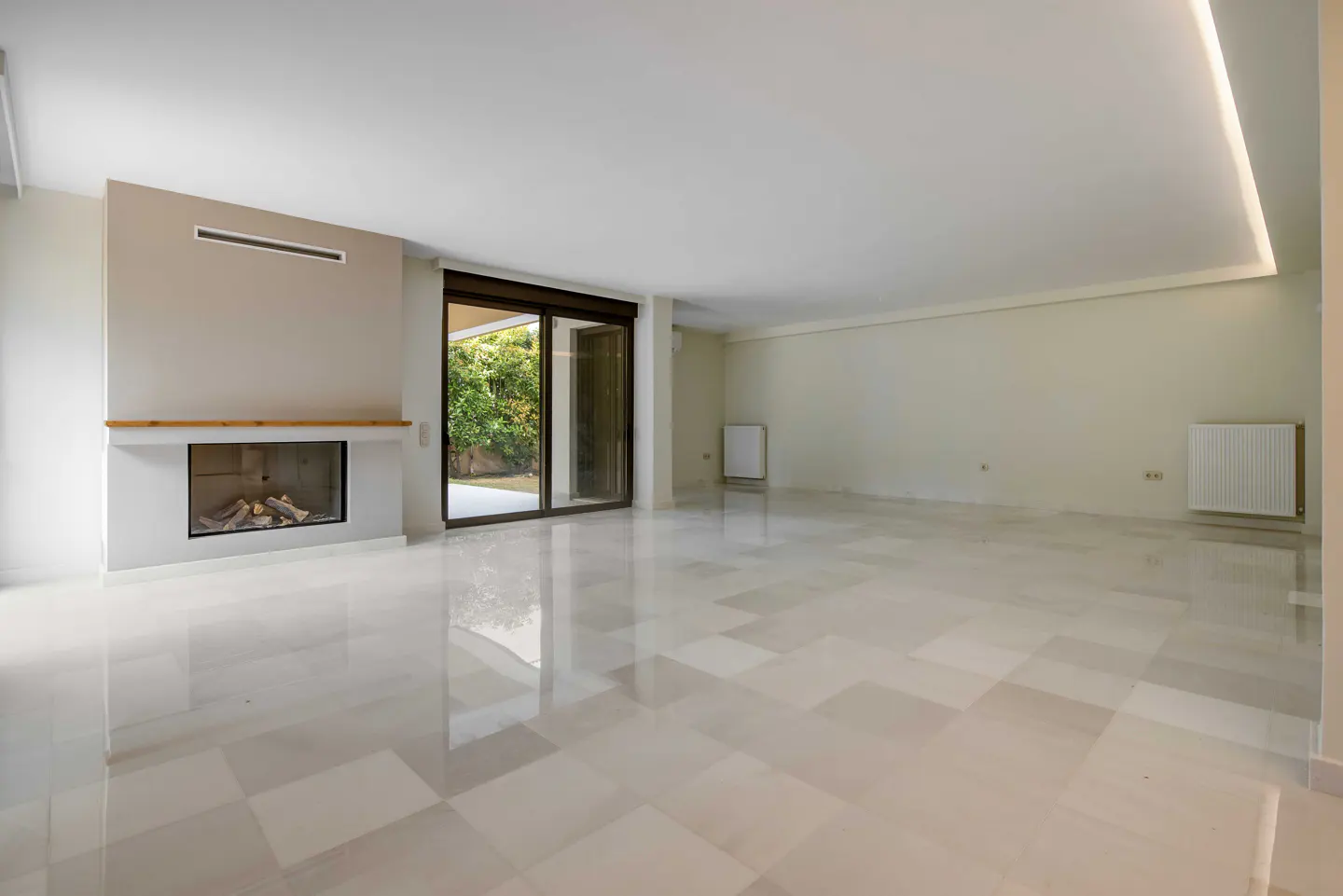 Bright, empty living room with marble floors, a fireplace, and sliding glass doors to a green yard.