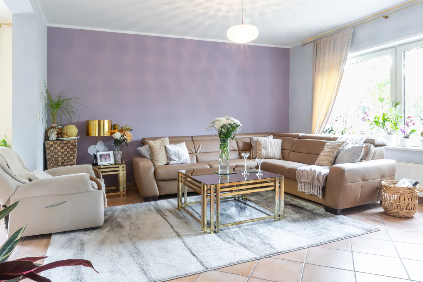 Living room with a brown leather sectional sofa, a gold coffee table, and a beige armchair on a gray and white rug.