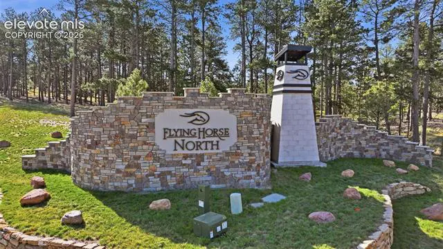 Stone entrance to Flying Horse North, with a tower and sign. The background is a forest with tall trees.