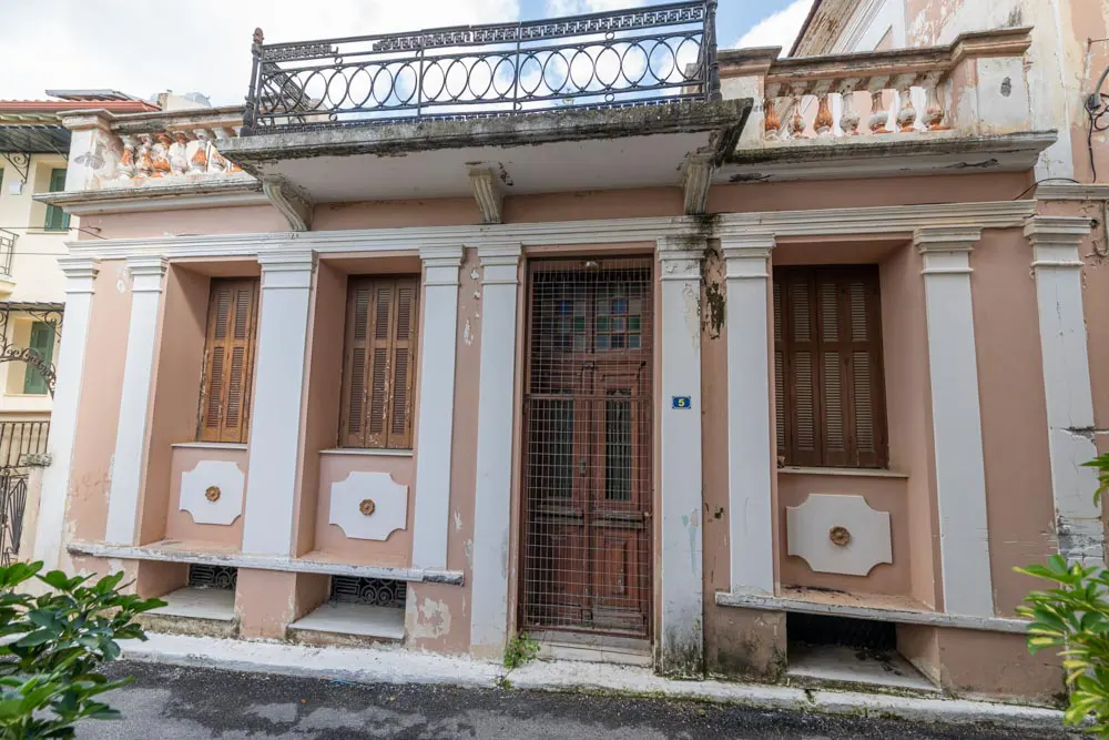 Exterior of a two-story pink building with white columns, brown shutters, and a metal balcony.