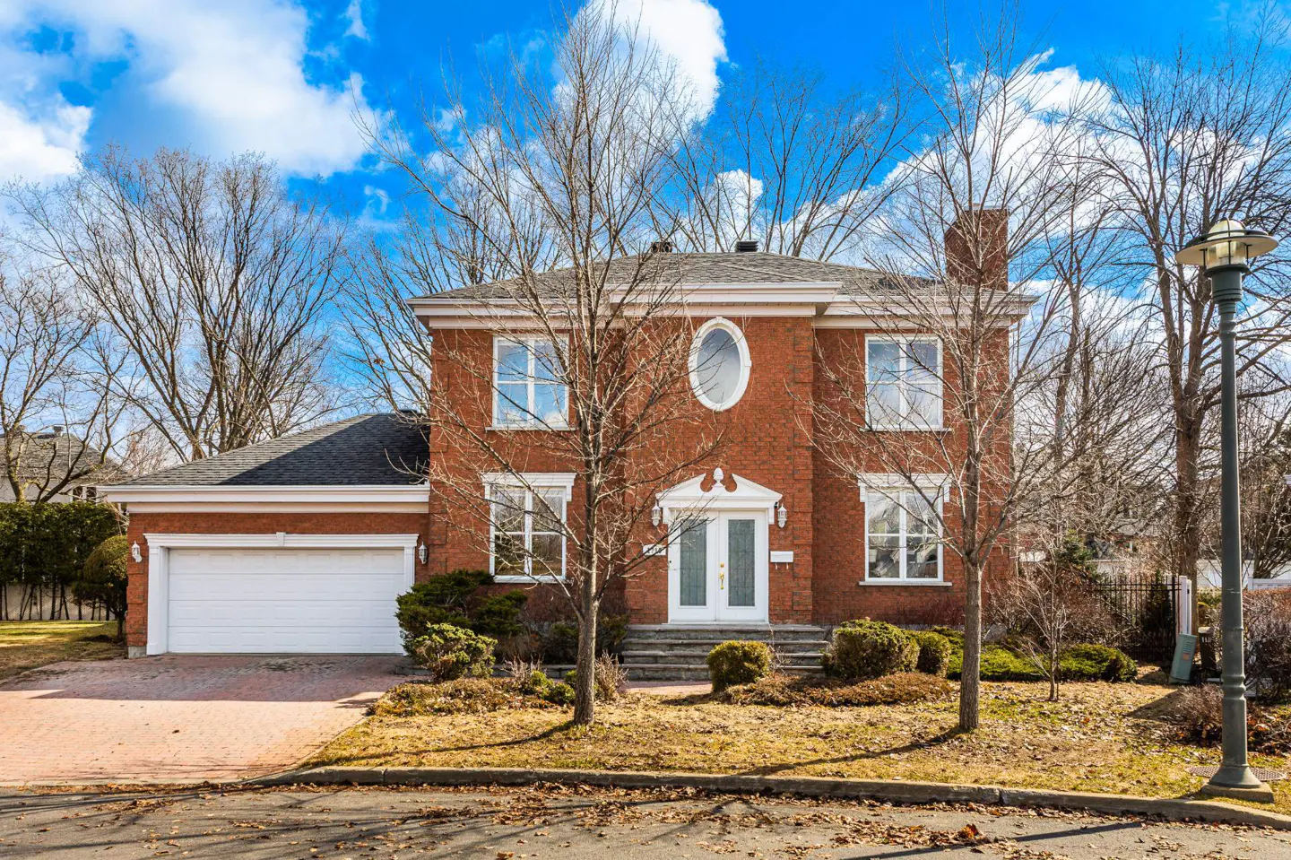 Two-story red brick house with white trim, a white garage door, and a black roof under a blue sky with clouds.