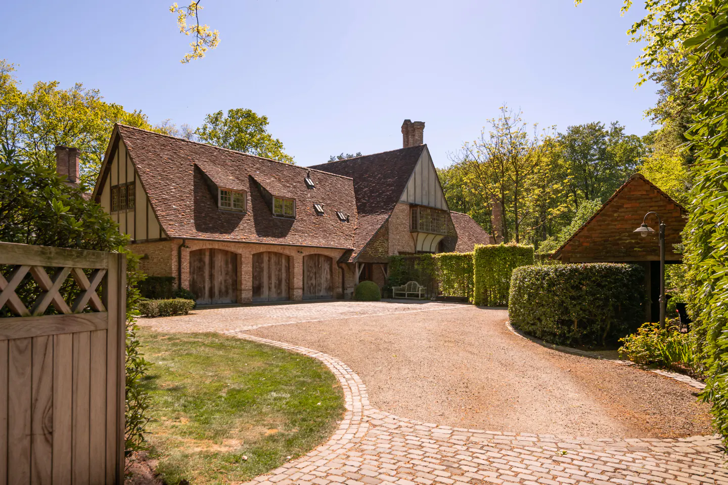 Exterior view of a large brick house with a brown tile roof, wooden garage doors, and a cobblestone driveway.