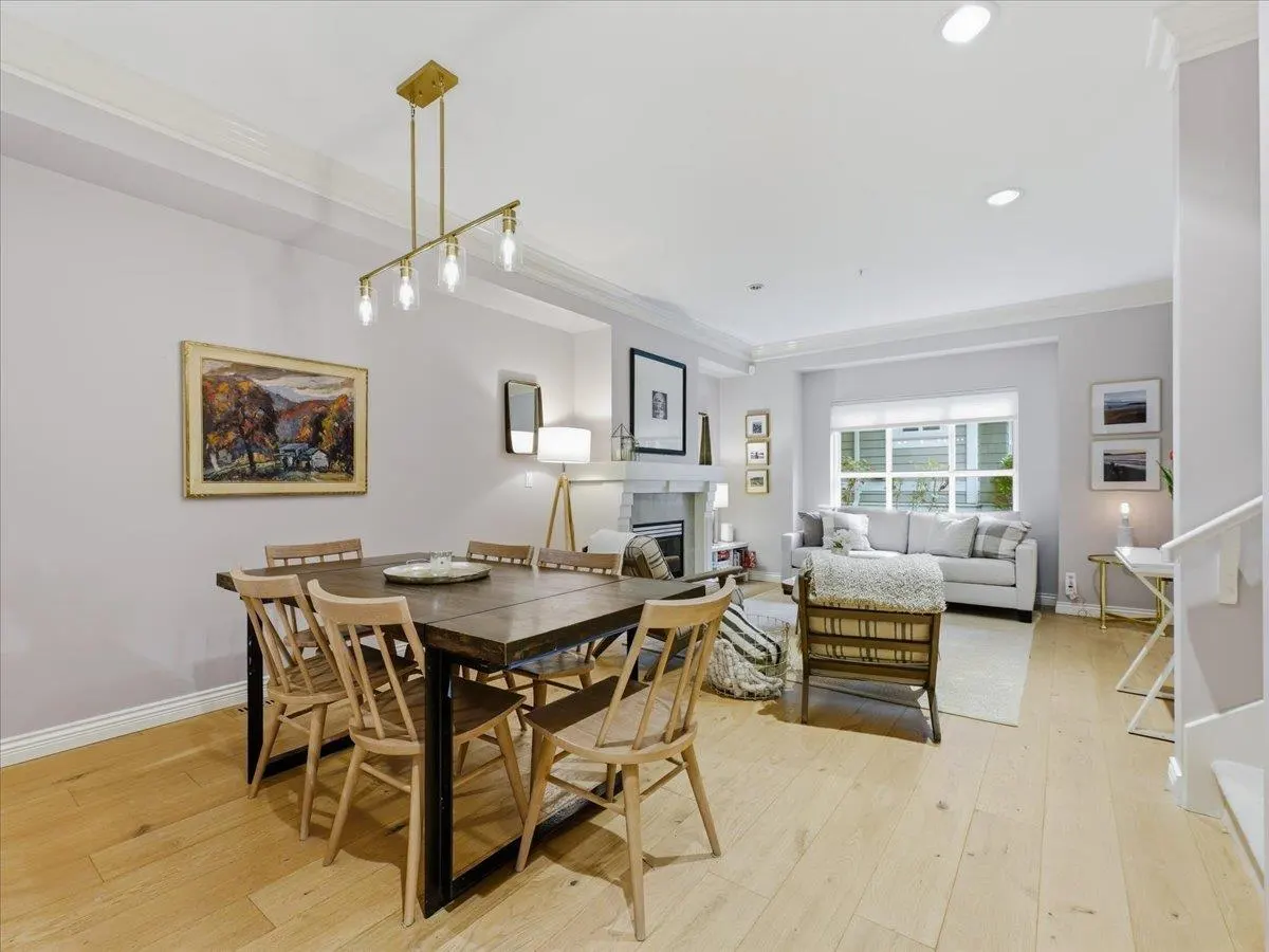 Open-concept living space with a dining table, chairs, and a living room with a sofa and fireplace. The walls are light gray.