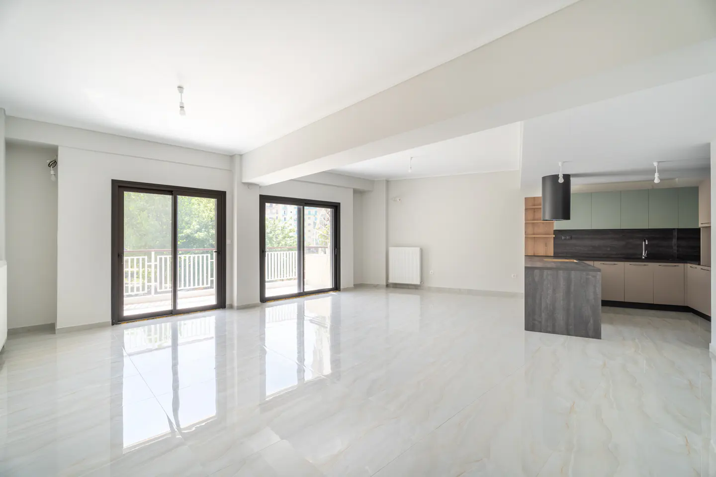 Bright, empty living room with white tile floors, two sliding glass doors to a balcony, and a modern kitchen in the background.