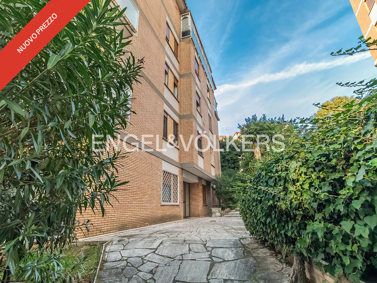 Exterior view of a brick apartment building with a stone walkway and green foliage. "Nuovo Prezzo" banner is visible.