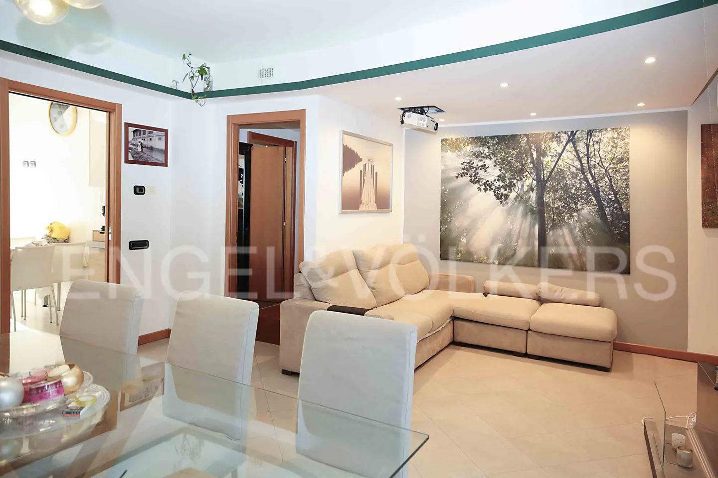 Living room with beige sectional sofa, glass dining table with white chairs, and a large tree art print.