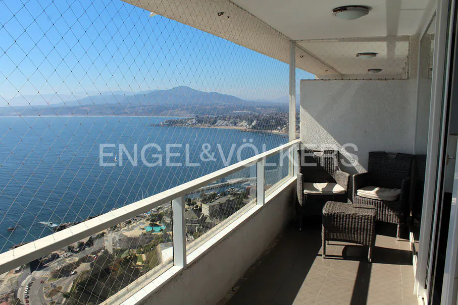 Balcony with wicker furniture overlooks a blue ocean and distant mountains, protected by a safety net.