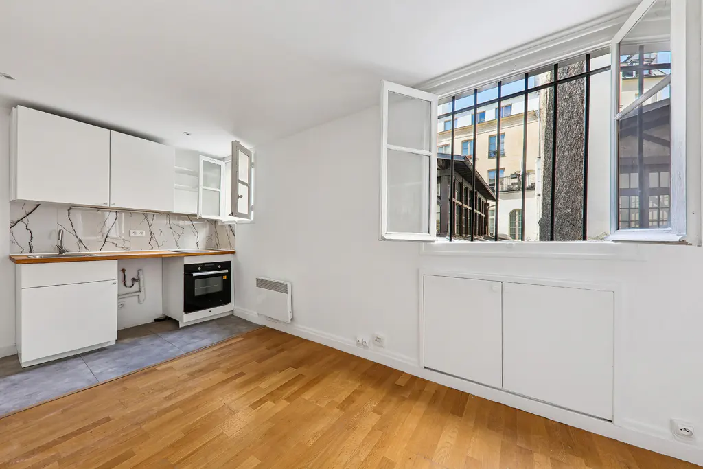 Minimalist kitchen with white cabinets, marble backsplash, and wood floors, featuring an open window with city views.