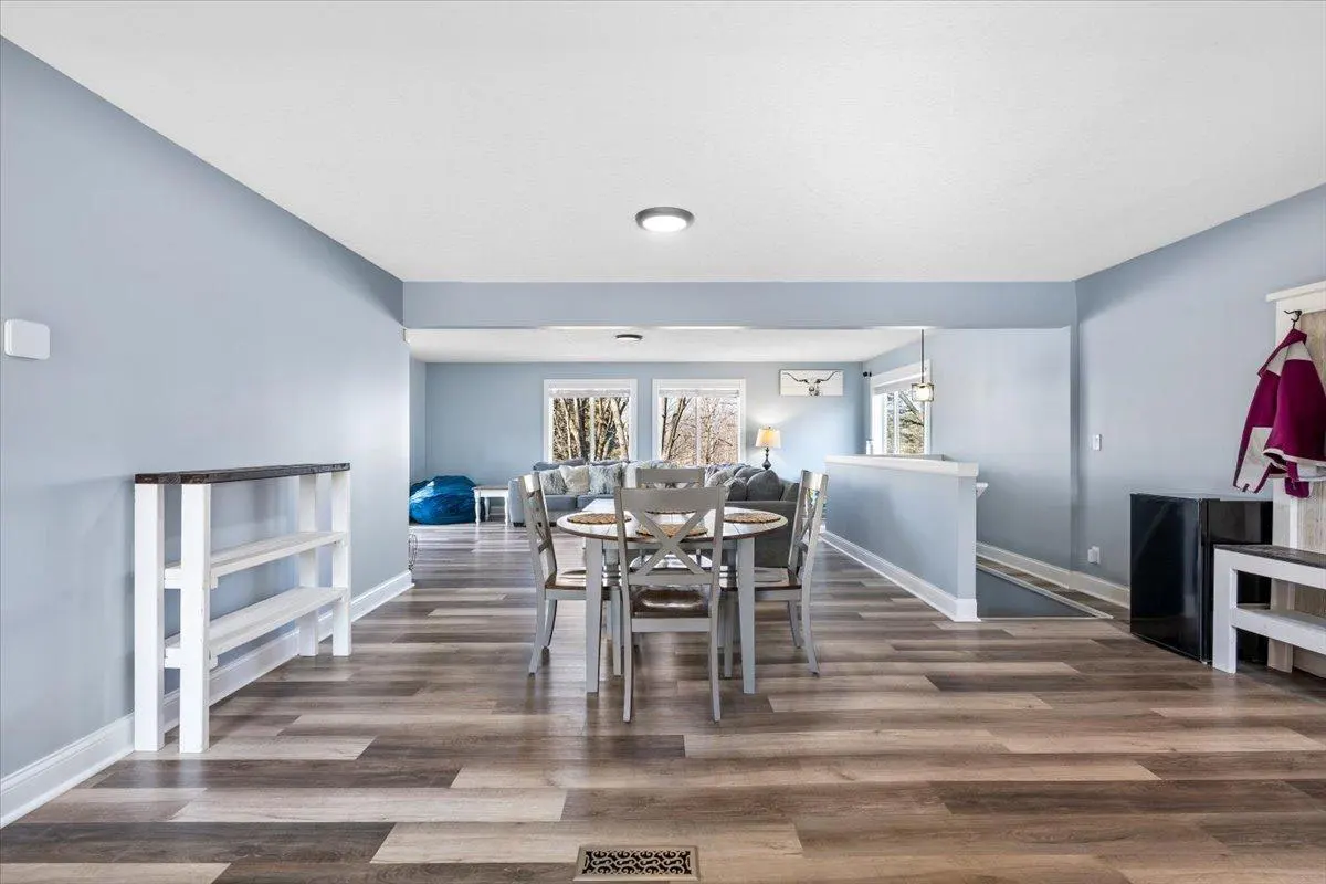 Open-concept dining room with light blue walls, wood floors, and a round table with four chairs. Living room visible in the background.