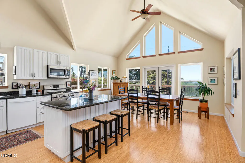 Bright, open kitchen and dining area with white cabinets, granite countertops, and a vaulted ceiling with large windows.