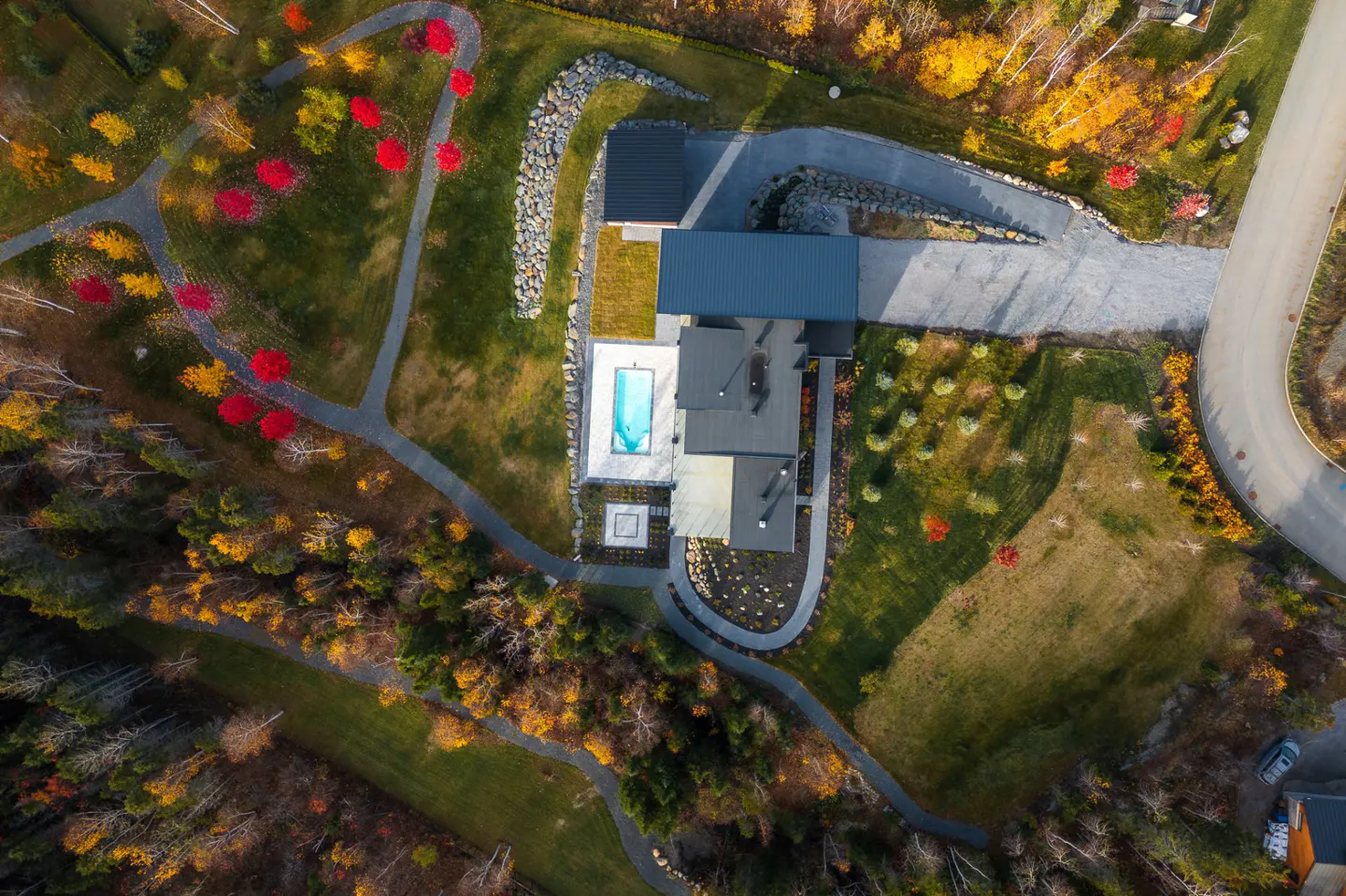 Aerial view of a modern house with a pool, surrounded by autumn foliage and winding paths.