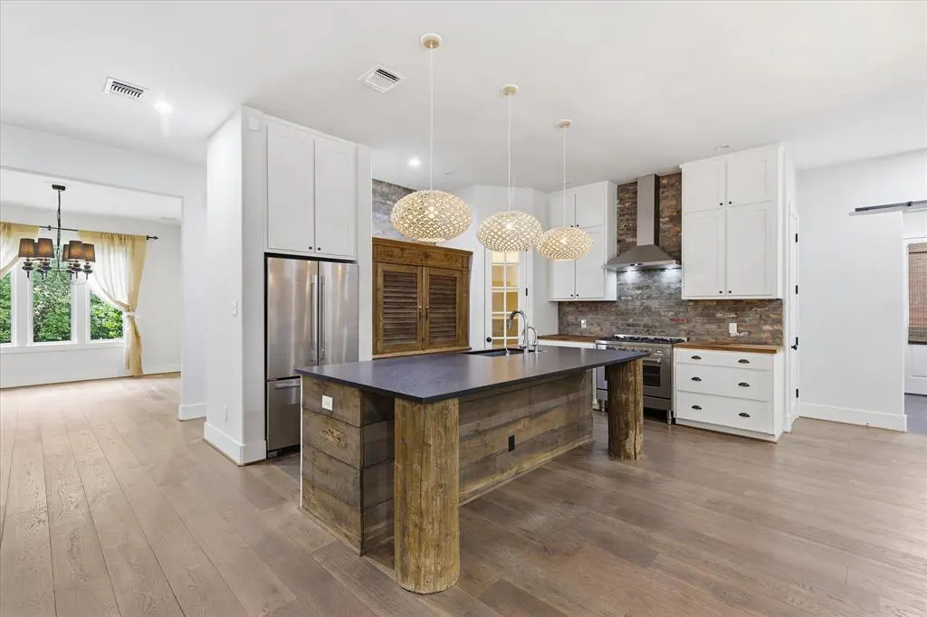 A modern kitchen with a wood island, stainless steel appliances, and white cabinets. Three pendant lights hang above the island.