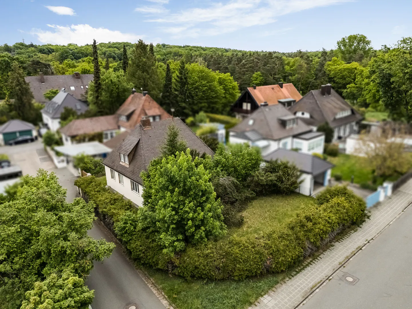Aerial view of a white house with a brown roof surrounded by green trees and bushes.