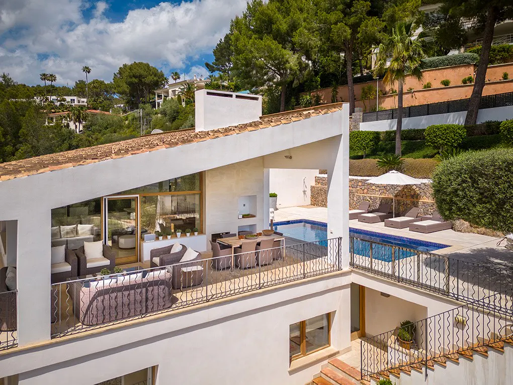 Aerial view of a modern white villa with a terracotta roof, featuring outdoor seating, a dining area, and a blue swimming pool.