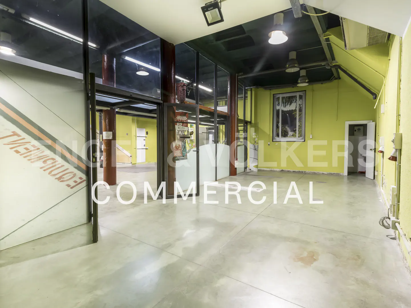 Spacious commercial interior with lime green walls, concrete floors, dark ceiling, and glass partitions.
