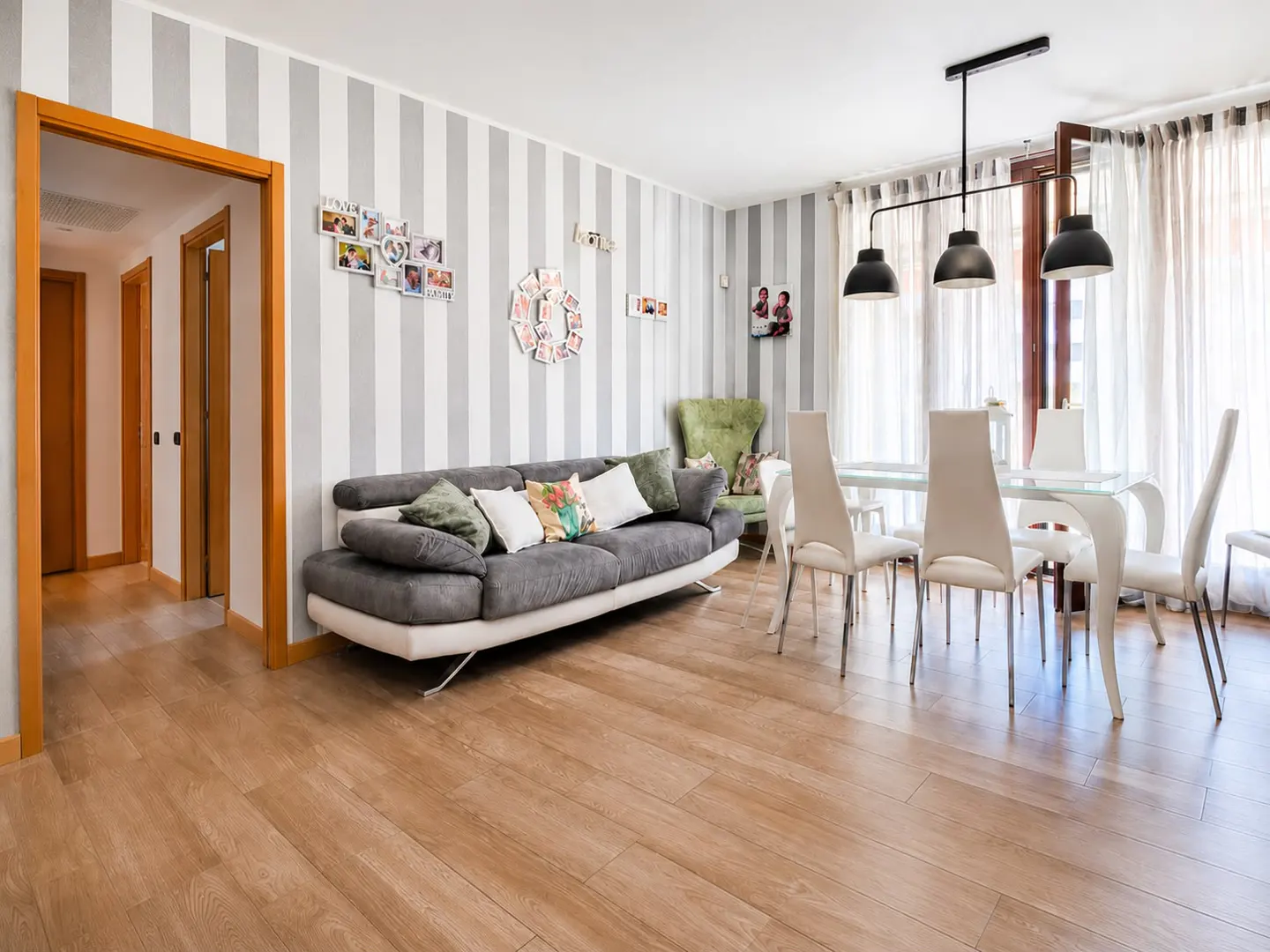 Living room with grey striped walls, a grey sofa, dining area with white chairs, and light wood floors.