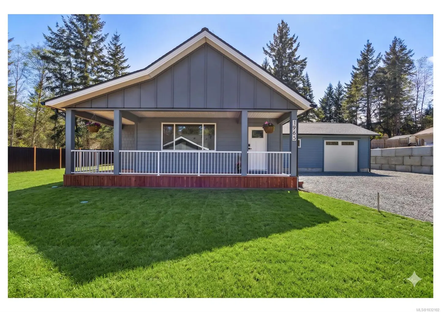 A gray house with a white porch railing and a green lawn on a sunny day.