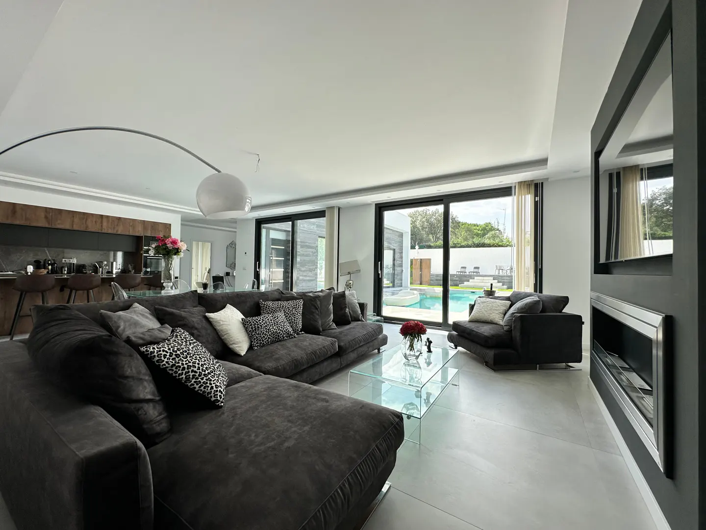 A modern living room with a gray sectional sofa, glass table, and view of a pool through sliding glass doors.