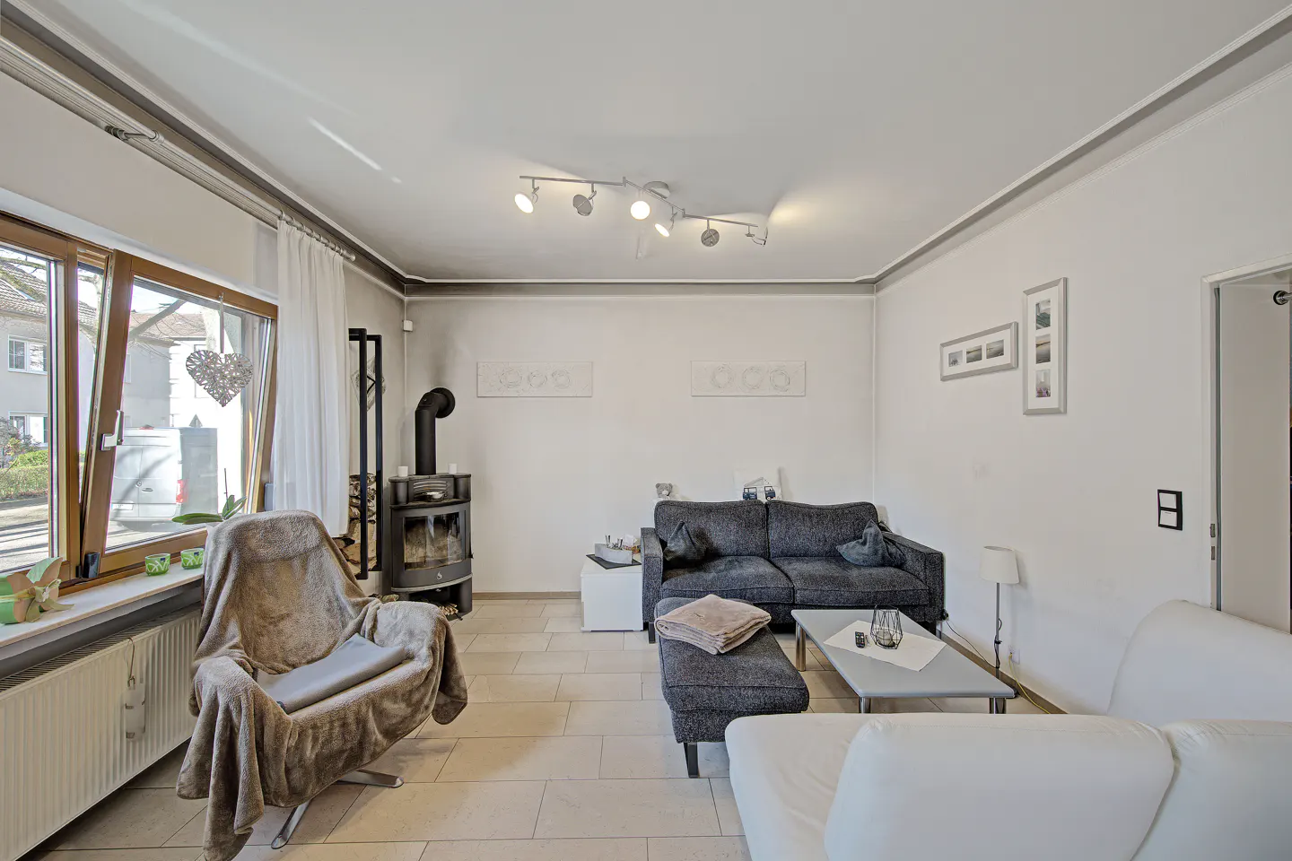 Living room with a wood-burning stove, gray sofa, white sofa, and a blanket-covered chair.