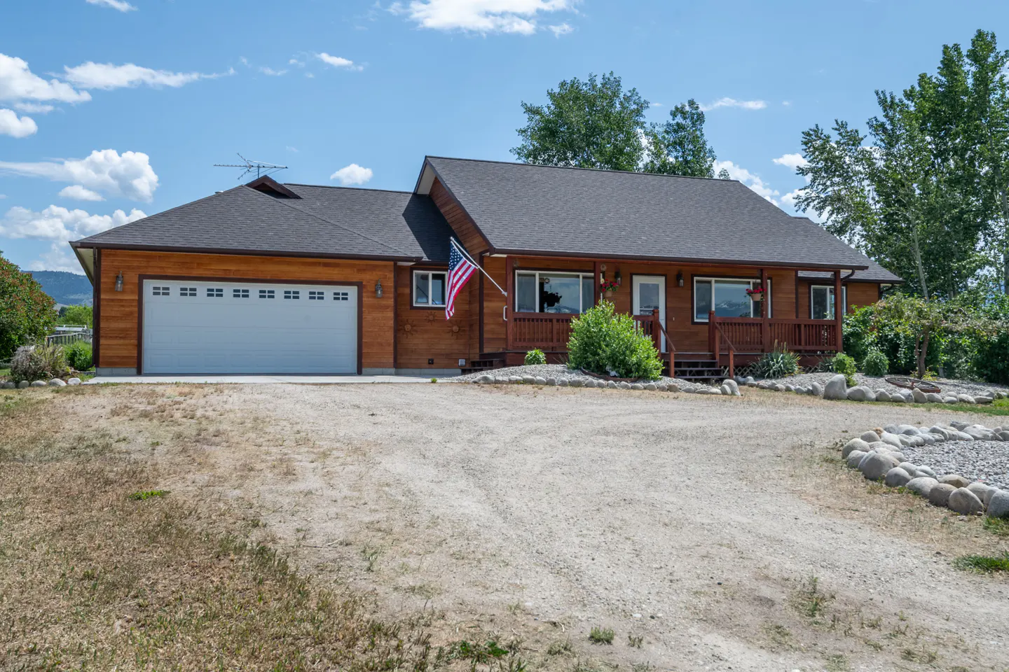 Exterior view of a one-story wood home with a gray roof, white garage door, and an American flag.