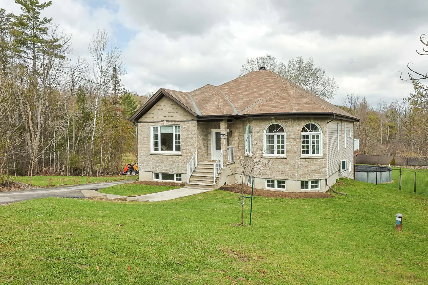 A tan brick house with a brown roof, white trim, and a green lawn on a cloudy day.