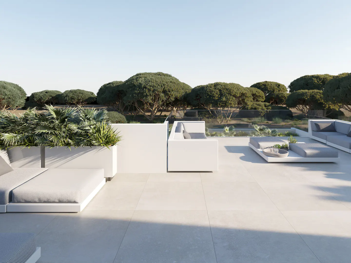 Outdoor patio with white lounge furniture, planters, and trees in the background under a clear blue sky.