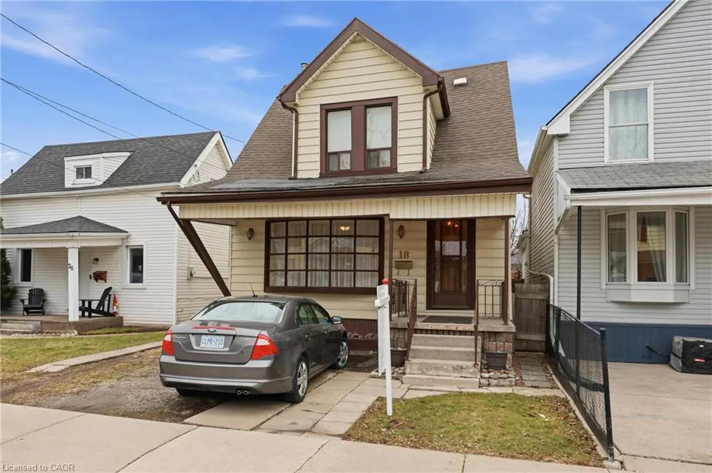 Two-story house with beige siding, brown trim, and a brown roof. A gray car is parked in the driveway. Other houses are visible.