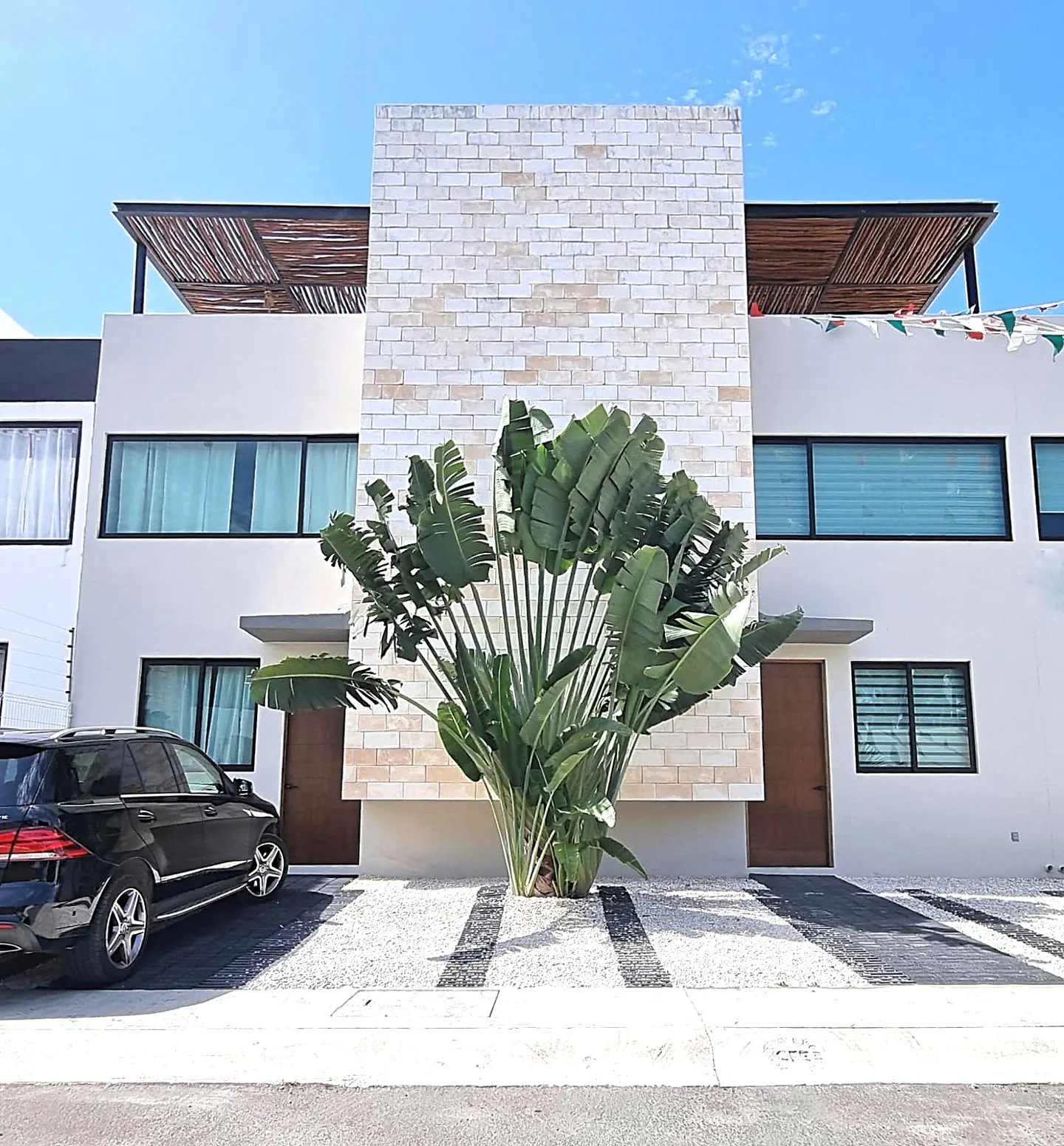 Modern white townhouses with a palm tree in front, a black car parked on the left, and a blue sky above.