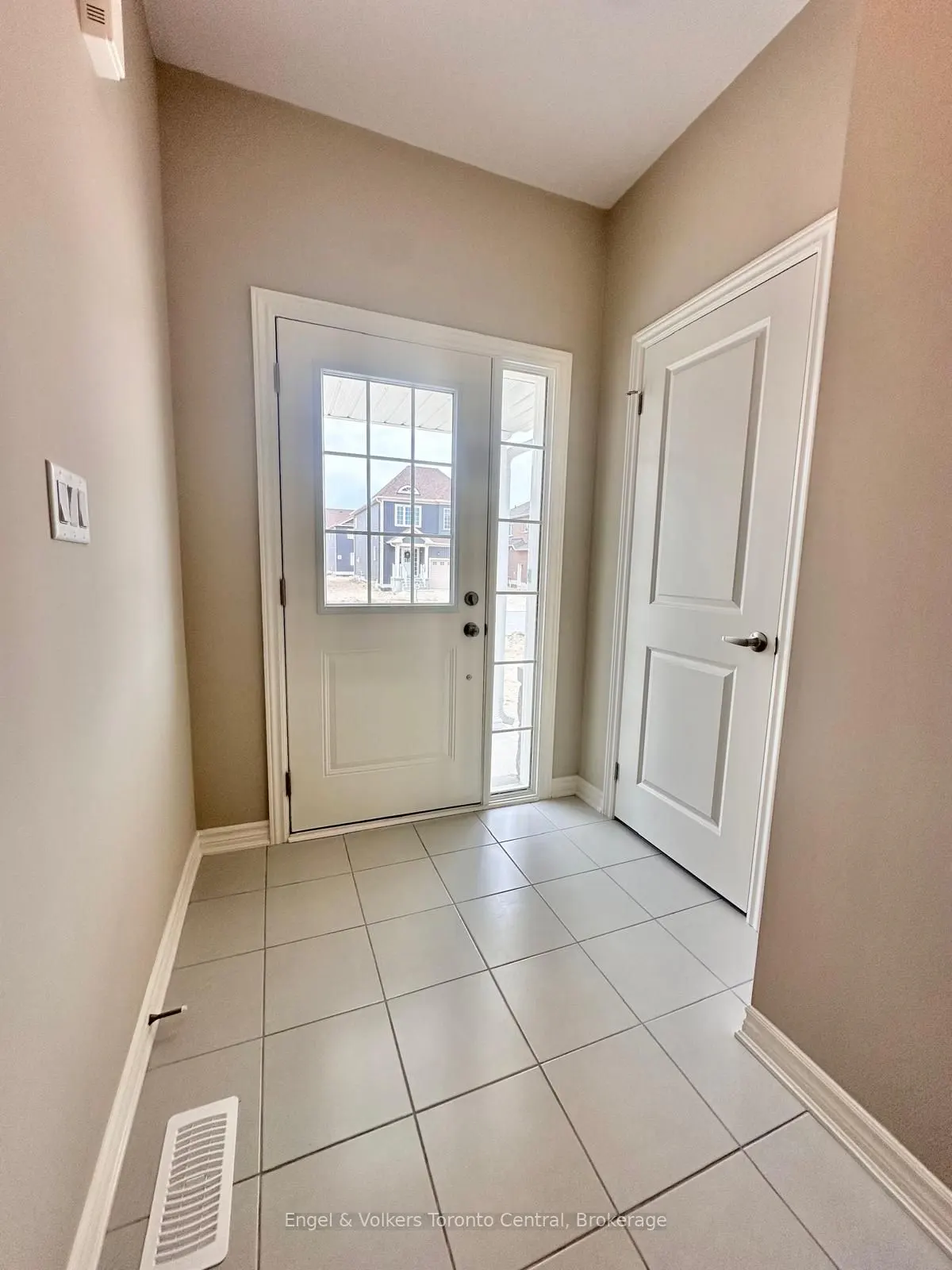Entryway with white door, sidelight, and grid window. Beige walls, white trim, and light tile floor. Another white door is to the right.