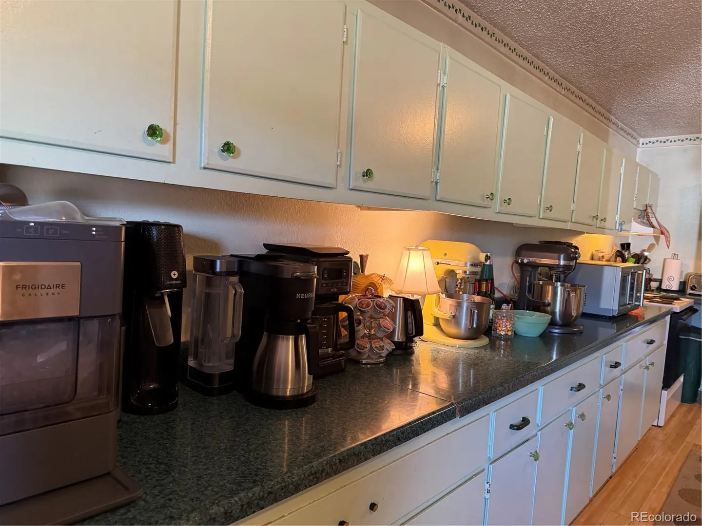 A kitchen counter with appliances, light green cabinets, and green knobs.